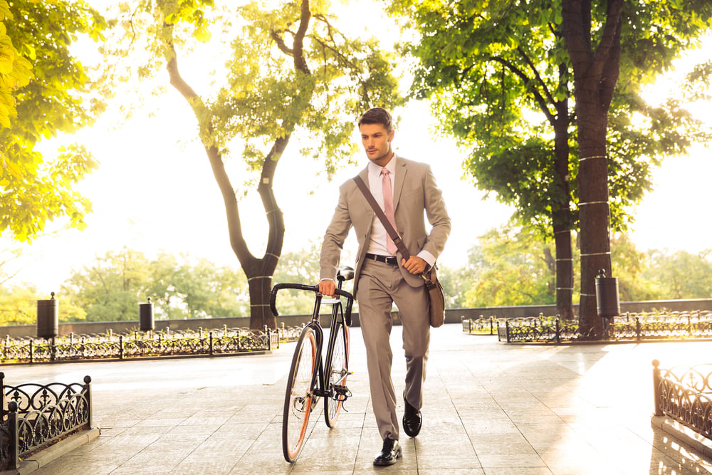 Confident young businessman walking with bicycle on the street in town
