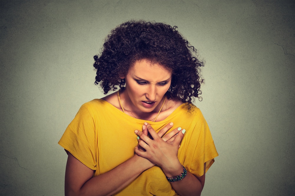 sick middle aged woman with heart attack, excruciating sudden pain, health problem holding touching her chest with hands isolated on gray background. Human face expression